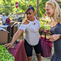 Two visitors browse fresh greens on a table