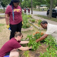 A garden expert assists two UAI youth tending a raised garden bed