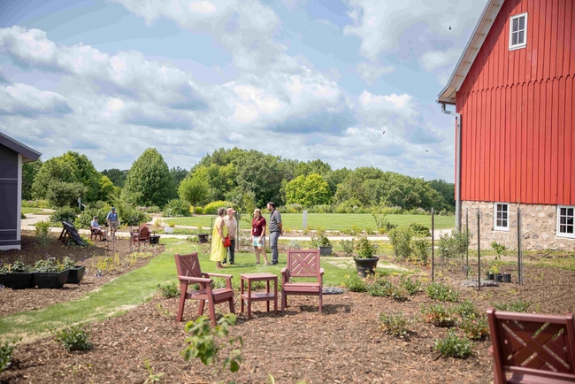 People mill about in the Foodscape area between the new building an the old red barn.