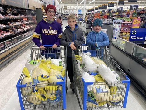 Three boys standing behind grocery carts filled with frozen turkeys.