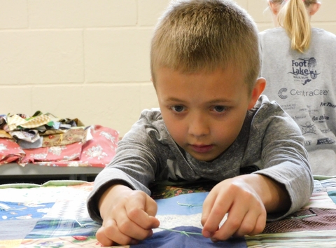 Young boy, maybe 5, ties a quilt square