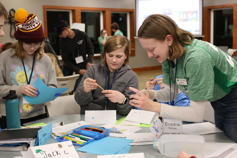 A 4-H state ambassador wearing an official green shirt helping youth members create desk name plates.