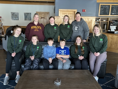 Two adults with a group of kids wearing 4-H shirts and smiling at the camera.