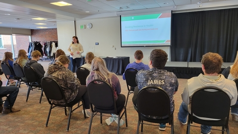 A woman presenting to a group of youth sitting in chairs.  