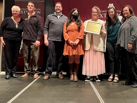 Welcoming Communities team of six stands on stage next to the dean, holding an award plaque