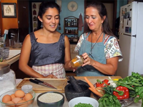 A young woman takes a jar from an older woman as they stand at a kitchen counter preparing food.