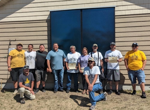 Group of adults standing in front to two installed solar panels on the side of a building.