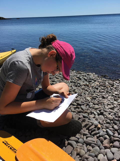 4-H youth writing on paper next body of water.