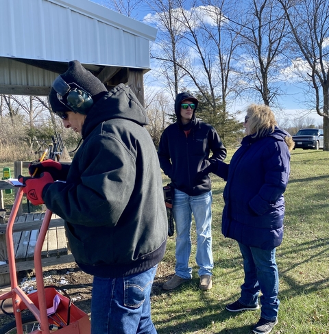 Adult 4-H volunteers standing outside with a youth member at a shooting sports and wildlife club meeting.