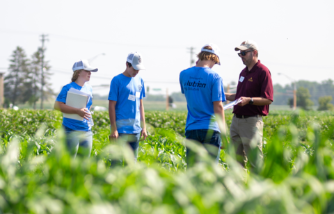 Three boys standing in a field talking to a man in an Extension polo.