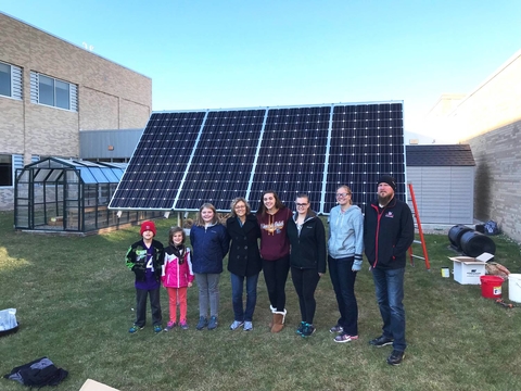 Students and teachers standing in front of a ground mounted solar panel.