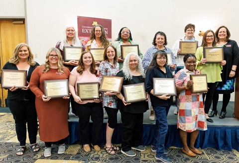 Group of 13 award winners holding plaques next to the dean of Extension