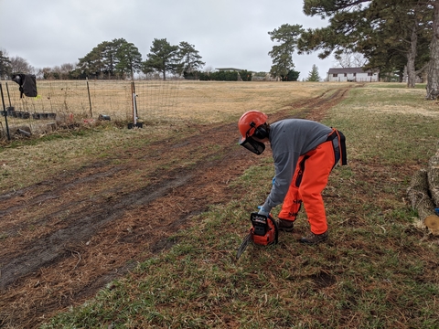 Person in personal protective gear setting a chainsaw on the ground safely.