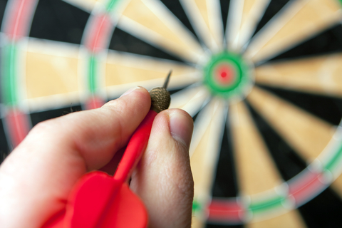 hand holding a dart aiming at a dartboard