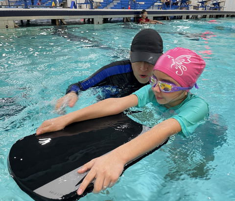 Youth with swimming instructor using a kickboard