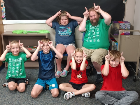 Youth members and a man holding up fingers by their heads to look like bug antennas while smiling at the camera. 