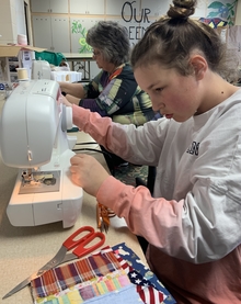 A young teen at the sewing machine with fabric and scissors