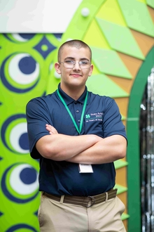 Participant crosses arms and looks at the camera with stage as backdrop