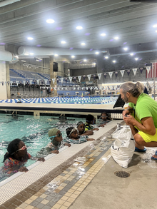 Six youth at an indoor swimming pool listen to instructor