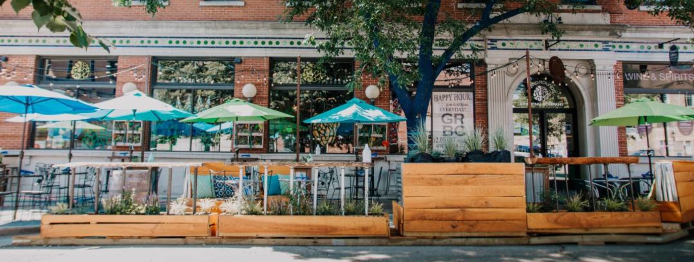 Dining space set up in the street in front of business, tables, chairs, Umbrellas, planters.