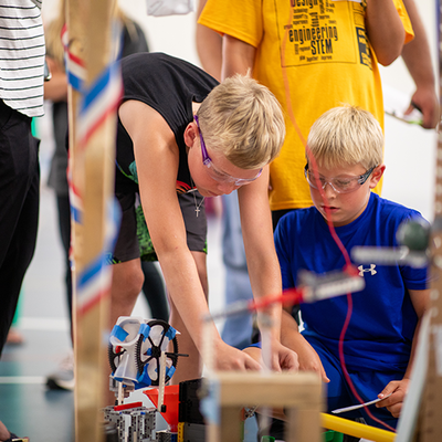 Two boys wearing safety goggles as they work on building the machine. 