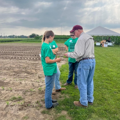 An older man talking with a small group of teens in a field.