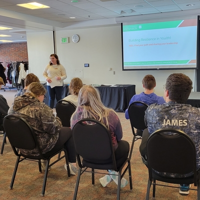 A woman presenting to a group of youth sitting in chairs.  