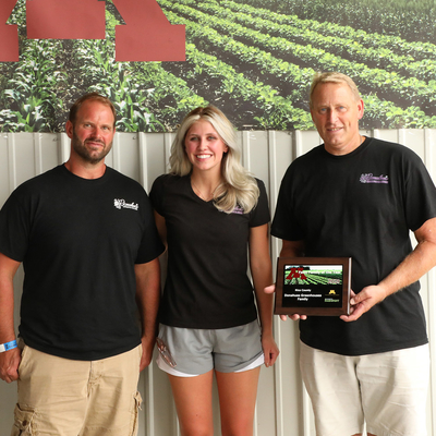 Members of the Donahue family (a woman and two men) pose in front of a "Farm Families of the Year" poster.