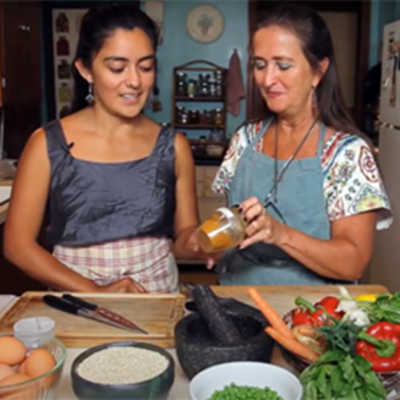 A young woman takes a jar from an older woman as they stand at a kitchen counter preparing food.