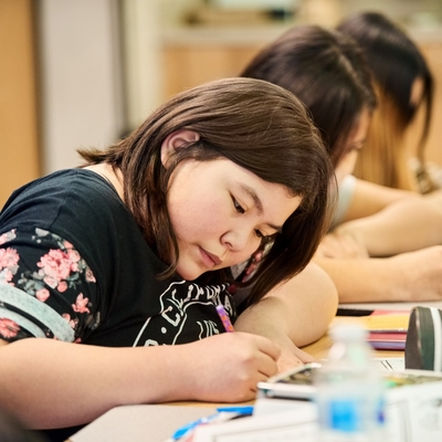 An Indigenous student is focused in the classroom writing.