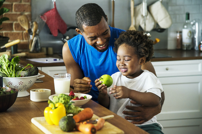 Father and young son eating fruit and vegetables at kitchen table