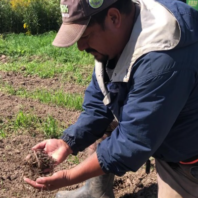 A man in a blue jacket stoops down to scoop soil from a field.