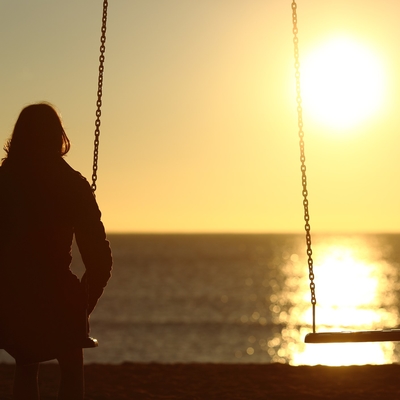 A person on a swing watching the sunset with an empty swing beside them. 