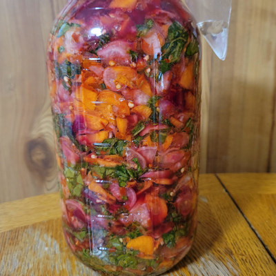 A glass jar filled with carrots, radishes and herbs fermenting. 