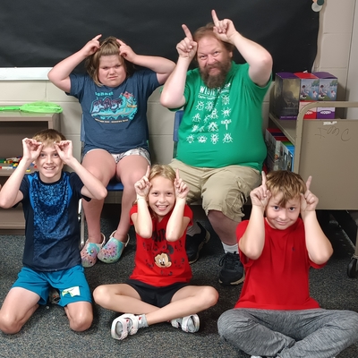 Youth members and a man holding up fingers by their heads to look like bug antennas while smiling at the camera. 